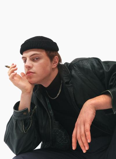 Gulyay-Pole Gopnik Core Крупний план: в'язана шапка, ланцюг поверх чорної водолазки, цигарка в пальцях і стьобана підкладка куртки