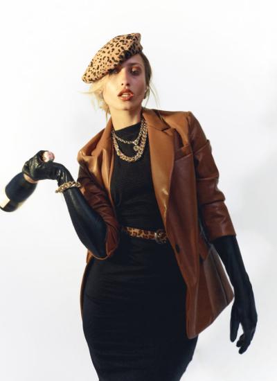 Leopard Accent Noir Коричневий шкіряний жакет поверх чорної сукні, леопардовий пояс, ланцюги на шиї і пляшка шампанського в руці