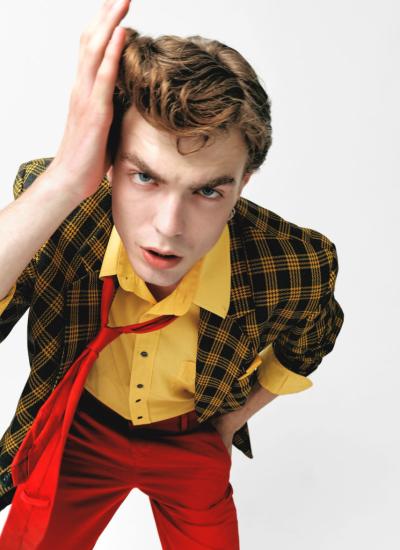 Mustard Grid & Crimson Flare Ракурс згори: рука в чубі, жовта сорочка, червона краватка-оселедець збилася набік, картатий піджак