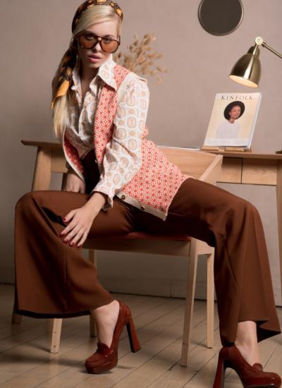 Seventies Fashion Classic Ноги врізнобіч на стільці біля столу з лампою: шоколадні штани-кльош, жилет у коралову мозаїку, бордові лофери на підборах